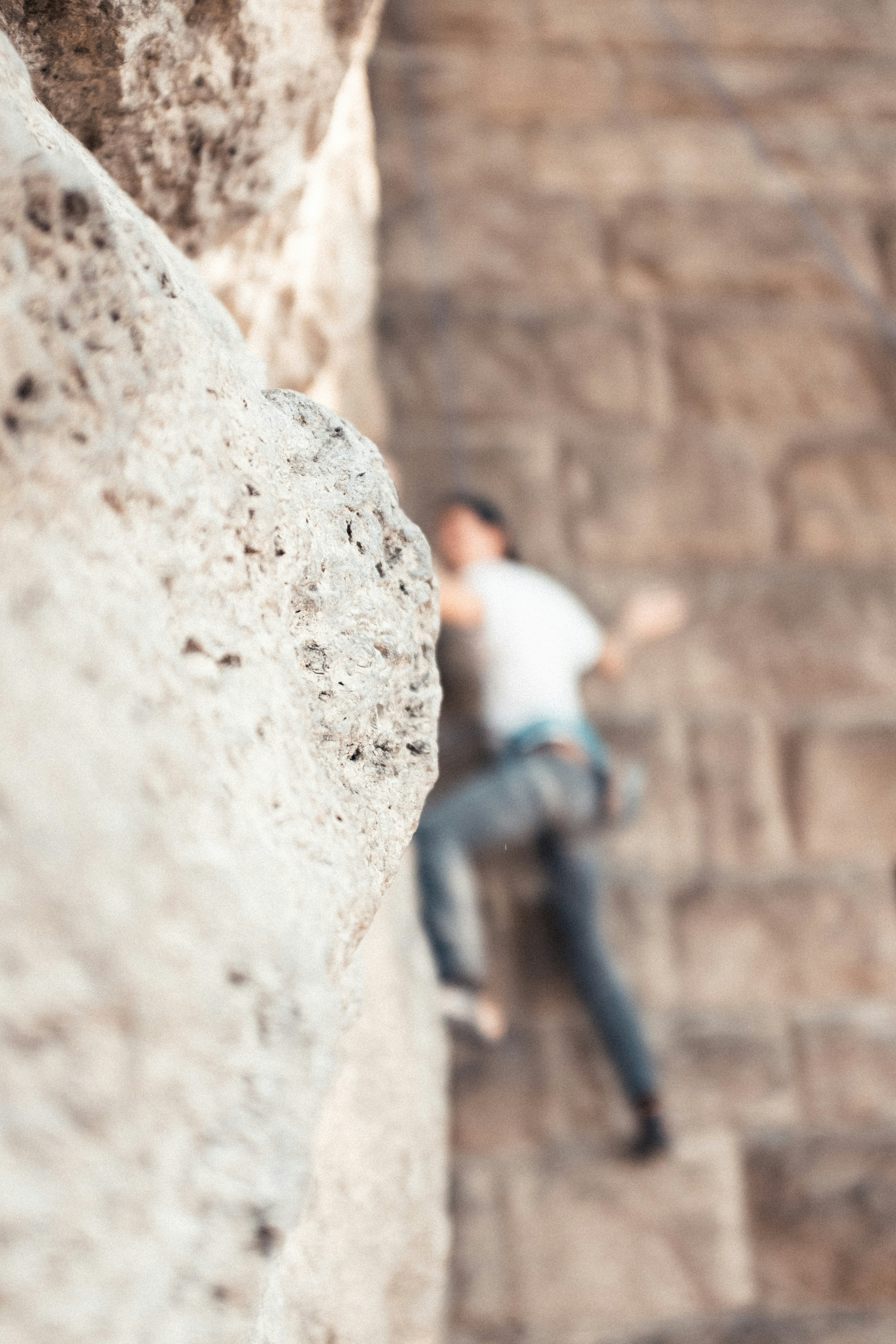 man in white t-shirt and blue denim jeans standing beside brown concrete wall during daytime